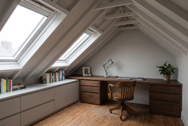 A home office in an attic with two roof windows, a built-in desk across the gable wall and low drawers under the eaves