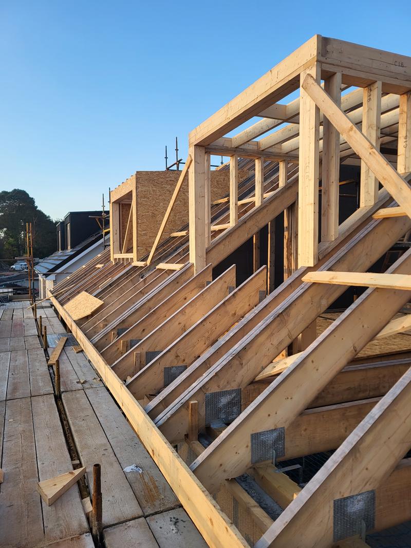 New timber dormer framing on a roof: rafters, a dormer front frame and joist hangers against a blue sky