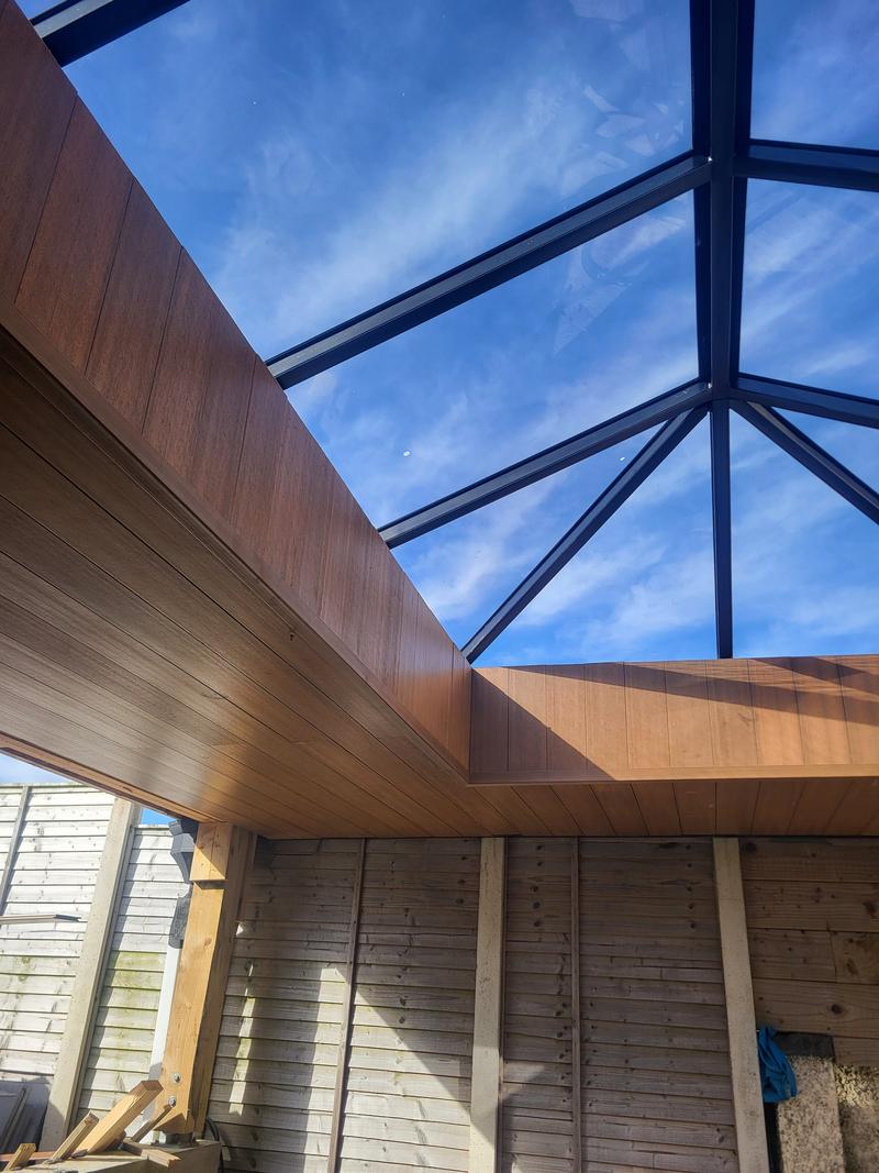 Timber-effect soffit boards around the opening of a lantern roof, with the glass roof and sky above