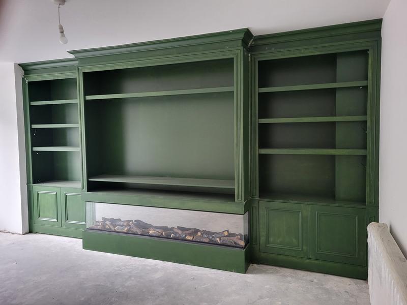 A painted green media wall: built-in bookcases either side, a recessed electric fire under a deep shelf, and panelled cupboard doors below
