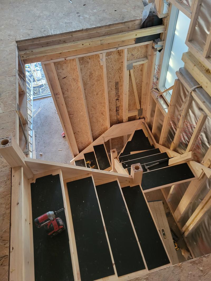 Looking down a staircase being fitted inside a timber frame build, the treads still covered with protective board