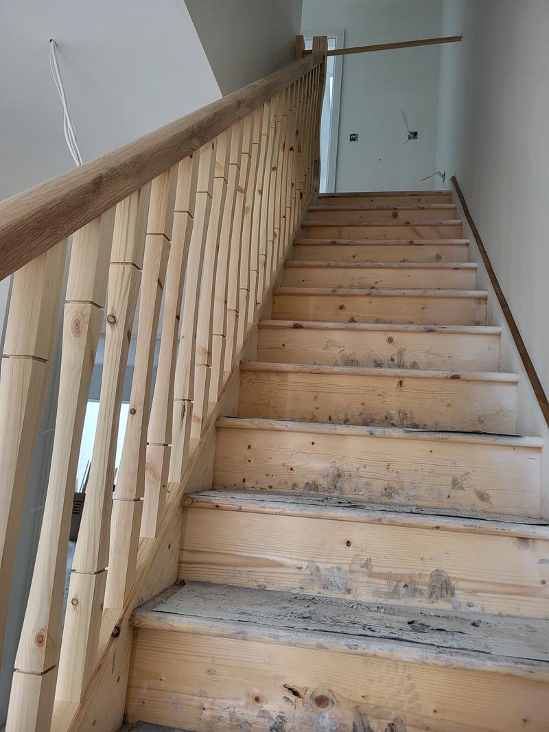 A new pine staircase with turned spindles and a handrail, looking up from the bottom step